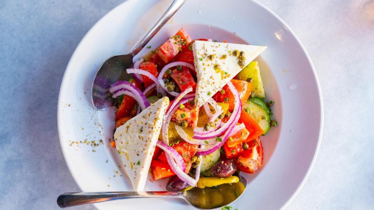 a colorful greek salad with triangle-shaped wedges of feta cheese sprinkled with greek spices