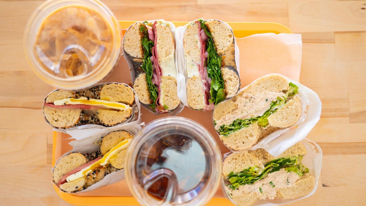 a light wood table with a tray of bagel sandwiches and iced coffee drinks on top, shot from above