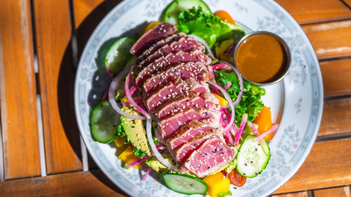 a fresh green salad with thin slices of raw ahi tuna decorated with sesame seeds on a blue and white china plate