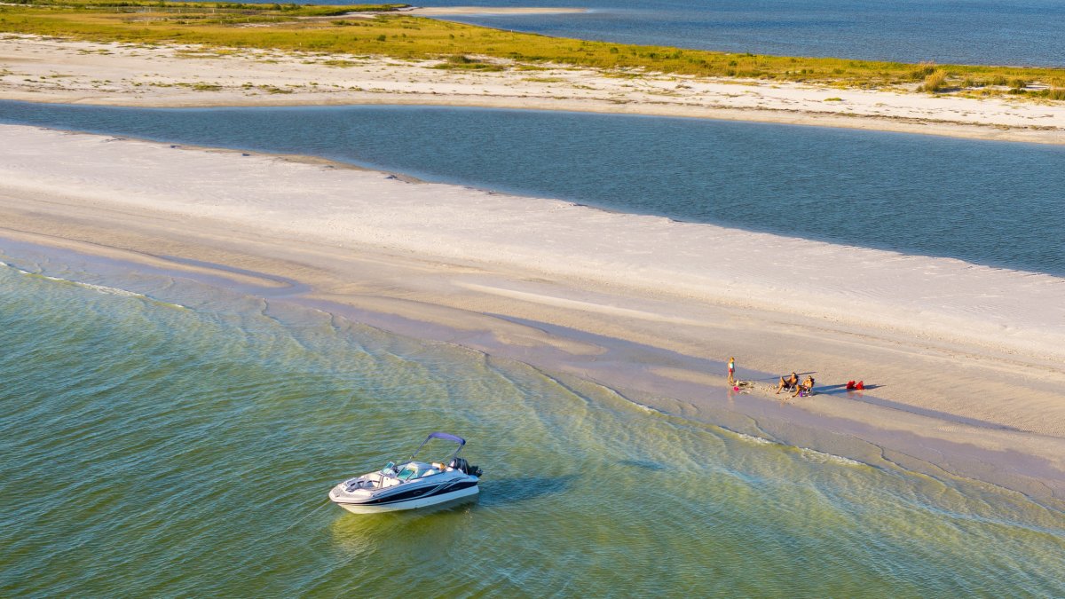 a boat at anchor near a small strip of land where people are relaxing on the beach