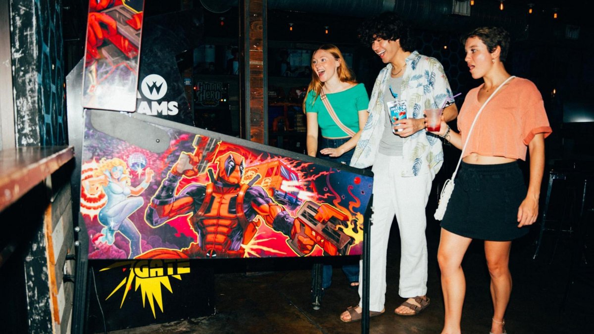 three young people play an arcade game at park