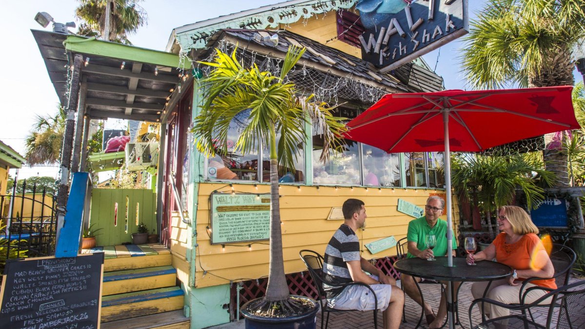 three people at an outdoor table with an umbrella at Walt'z Fish Shak at John's Pass Village & Boardwalk in Madeira Beach