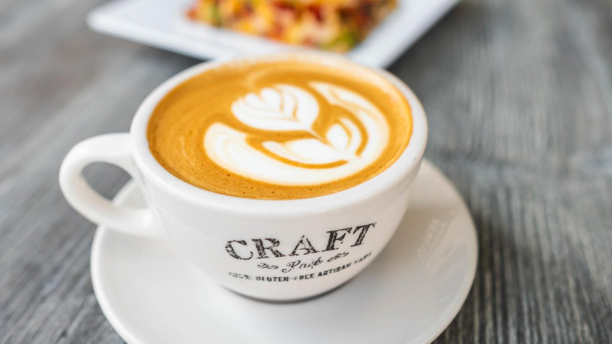 cappuccino with a flower design in a small white mug on a plate, next to a plate of food at Craft Kafe