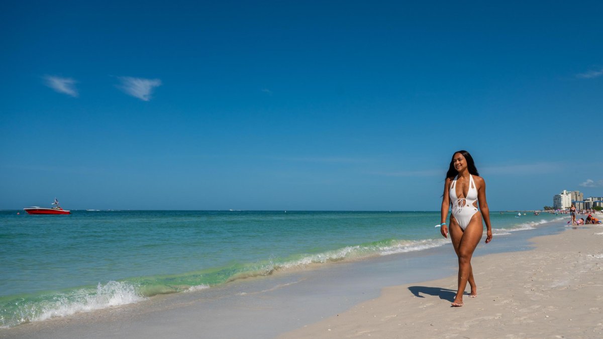 a young woman in a white bathing suit walks on the edge of the water at Clearwater Beach
