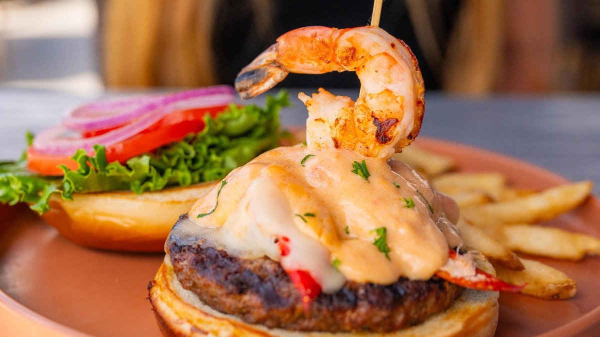 a burger with melted swiss cheese lobster and shrimp on a terra cotta colored plate at Sloppy Joe's in Treasure Island.