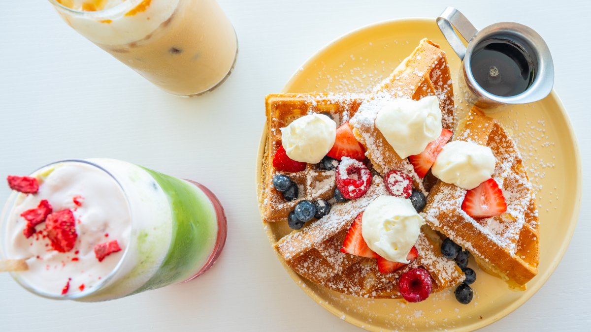 two colorful iced espresso drinks next to a plate of waffles topped with berries at Sugar Baby in Seminole