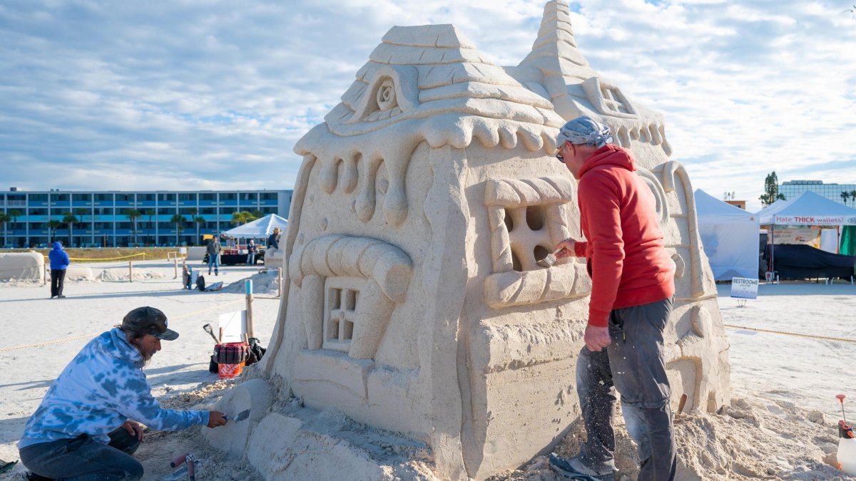 two artists work on a sand sculpture of a house at Sanding Ovations