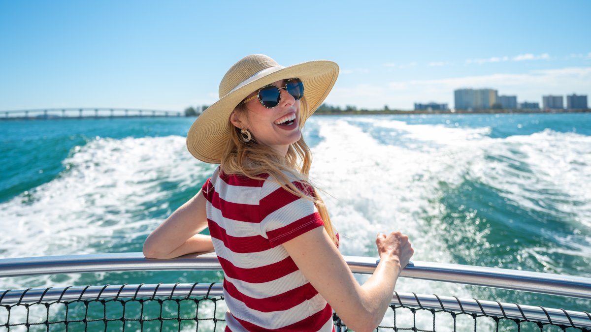 a smiling woman in a red and white striped shirt, sunglasses and a big hat at the back of the Little Toot sightseeing boat