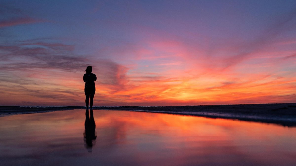a woman stands on the beach and watches a brilliant sunset in St. Pete-Clearwater