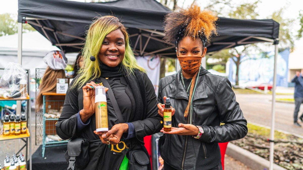 Two women wearing black outfits holding bottled products smiling.