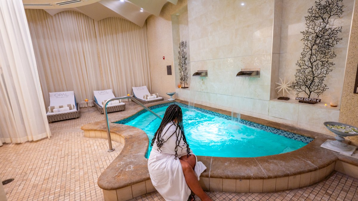 a woman in a spa bathrobe sitting on the edge of a small pool indoors at Opal Spa at Sandpearl Resort