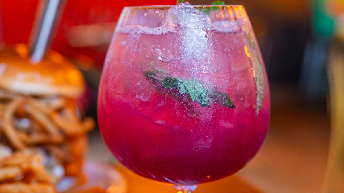 a bright pink cocktail with mint leaves next to a decadent burger at Gigglewater's