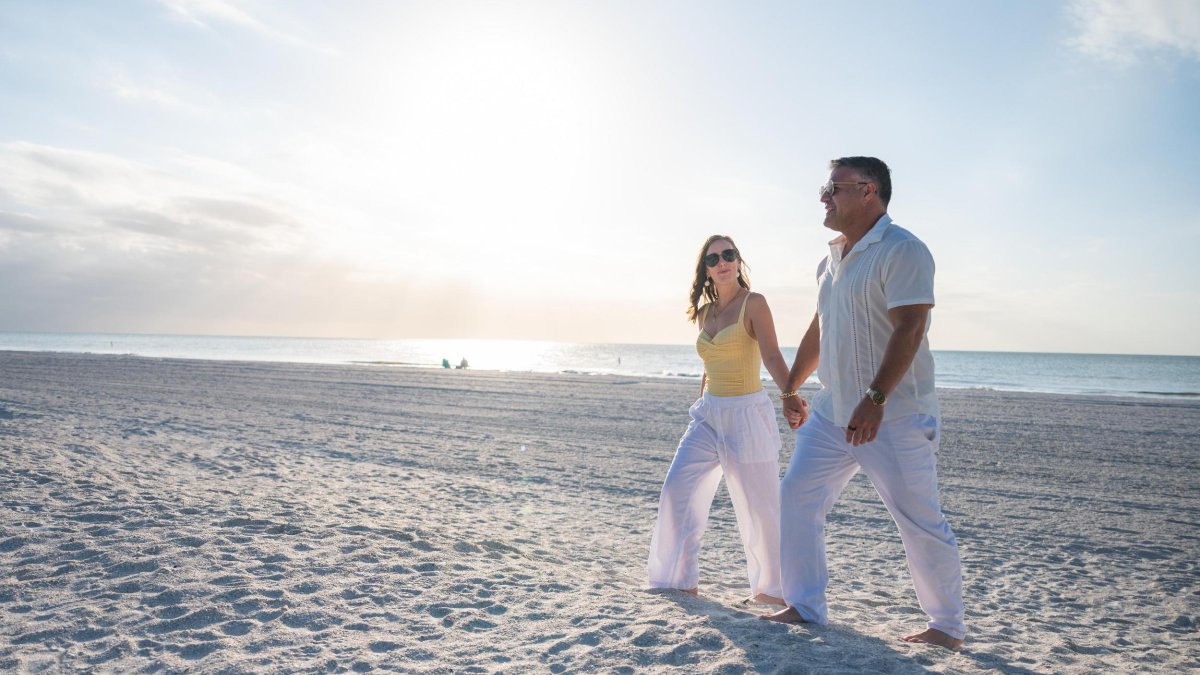 a couple walks holding hands on a white sand beach in St. Pete-Clearwater