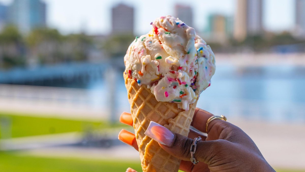 a woman's hand with a fancy manicure holding a waffle cone with ice cream and sprinkles at Driftwood Cafe at the St. Pete Pier