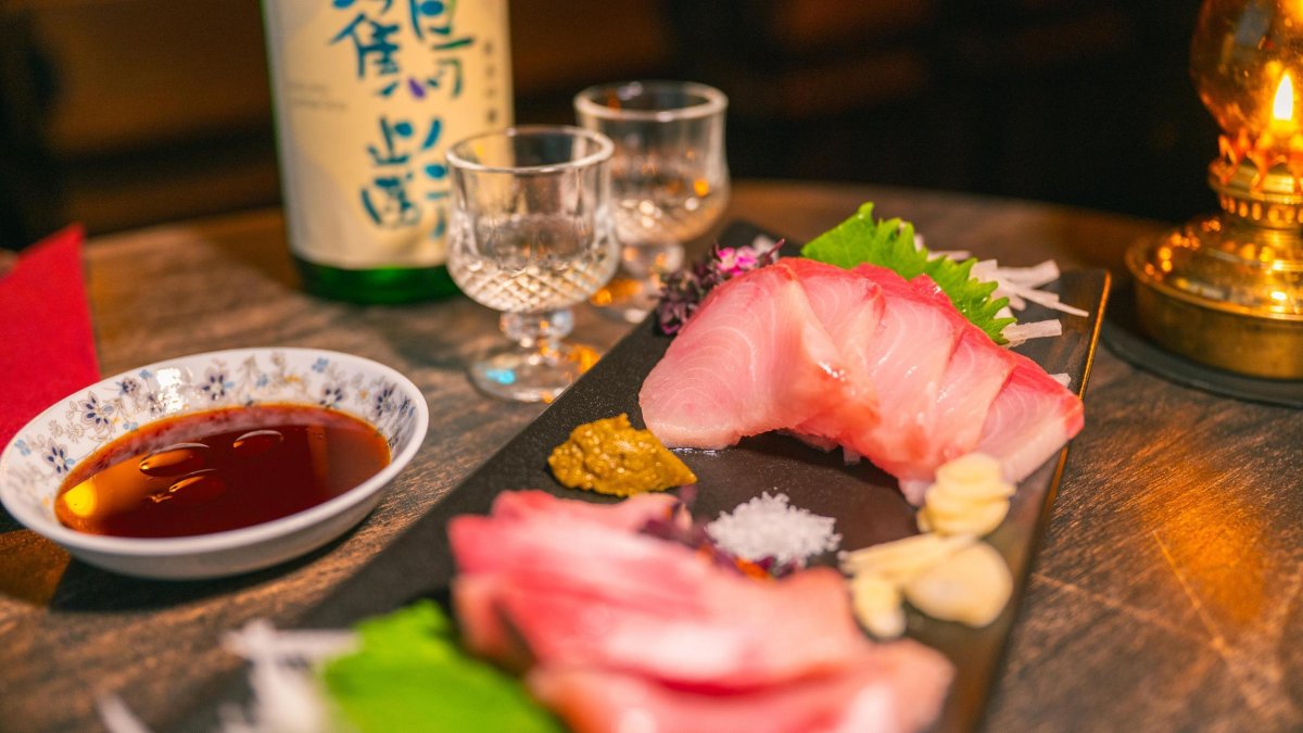 sashimi with a dipping sauce and glasses of sake at In Between Days in St. Petersburg FL