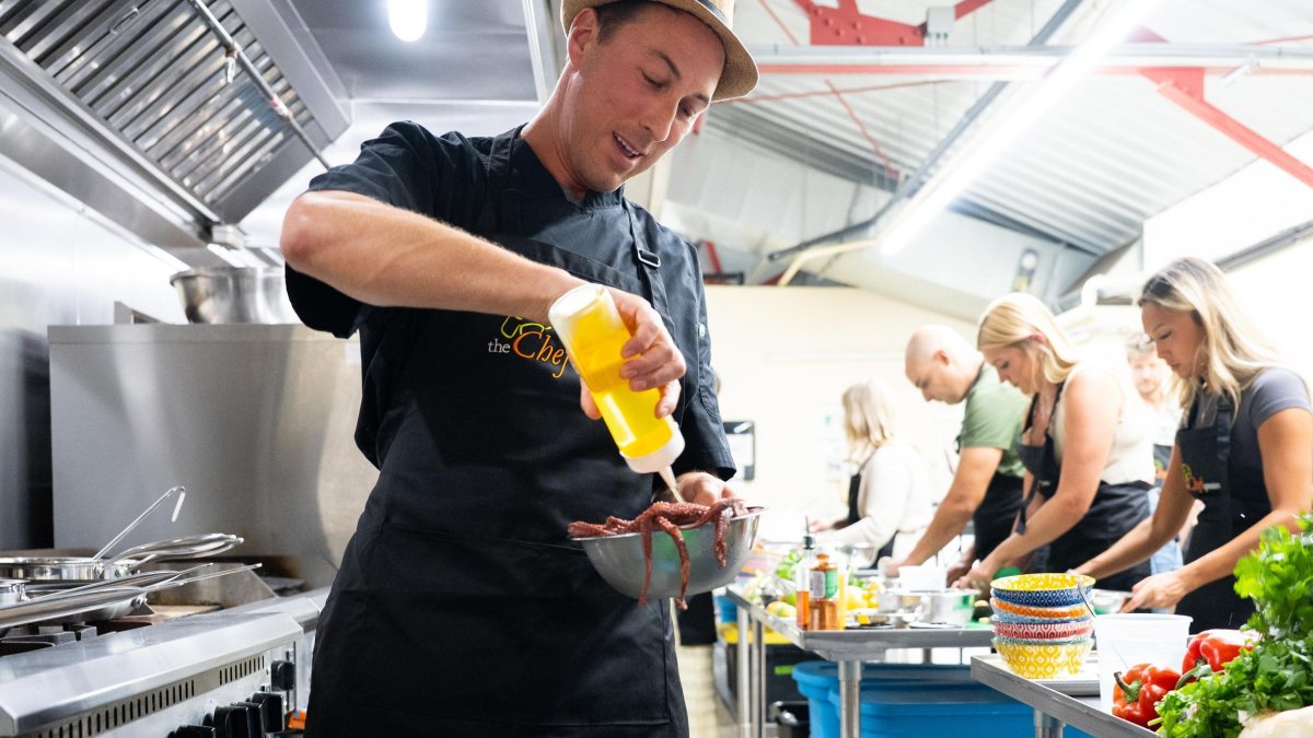 a chef adds oil to a bowl while students work in the background at a cooking class with The Chef Upstairs