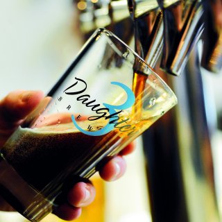 A person pouring dark beer in a 3 Daughters Brewery glass.