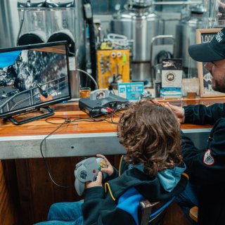 A man and boy play an old-style videogame inside a brewery.