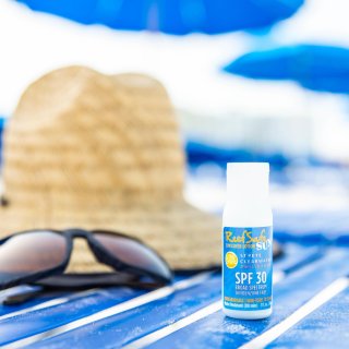 a beach towel with a straw hat, dark sunglasses and a small bottle of reef-safe sunscreen