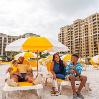 a famly relaxes on lounge chairs at the beach with the Sandpearl Resort in the background