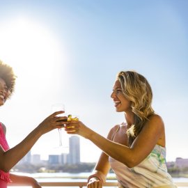 two women toast with cocktails at Pier Teaki rooftop bar at the St. Pete Pier
