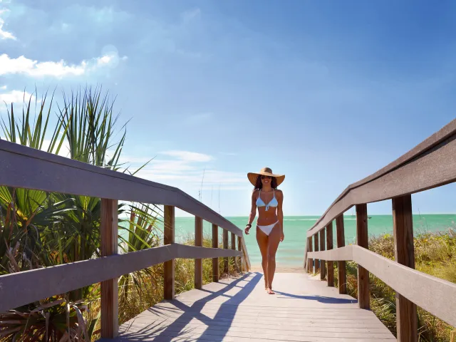 A young lady dressed in bikini walking Indian Rocks Beach boardwalk.