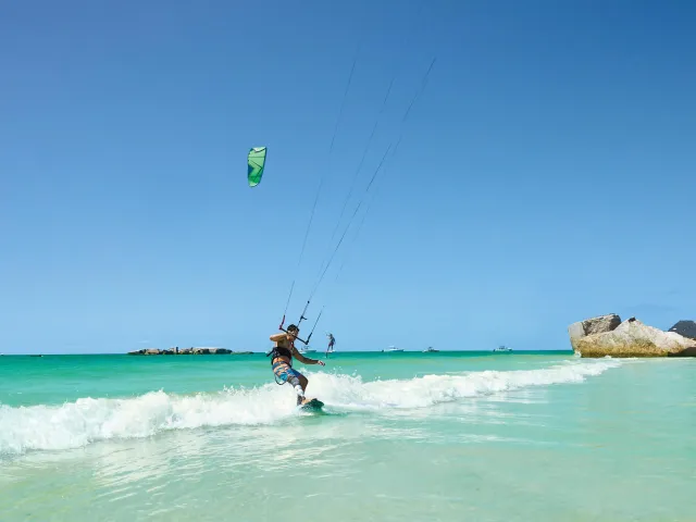 A man kitesurfing off Egmont Key. The water is emerald green with small waves and the ruins of Fort Dade can be seen.