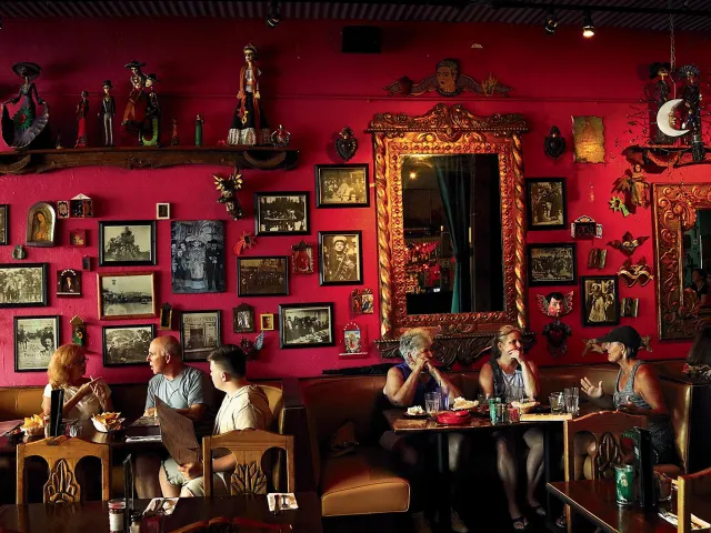 Six dinners eating at Casa Tina restaurant in Dunedin. The wall is red and decorated with multiple portraits.