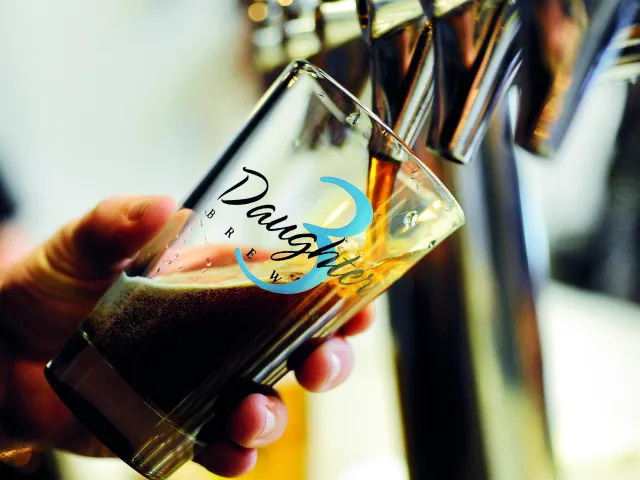 A person pouring dark beer in a 3 Daughters Brewery glass.
