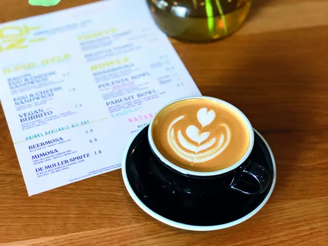 a cup of cappuccino with a pretty foam design in a black cup and saucer next to the menu for Bandit Coffee in St. Pete