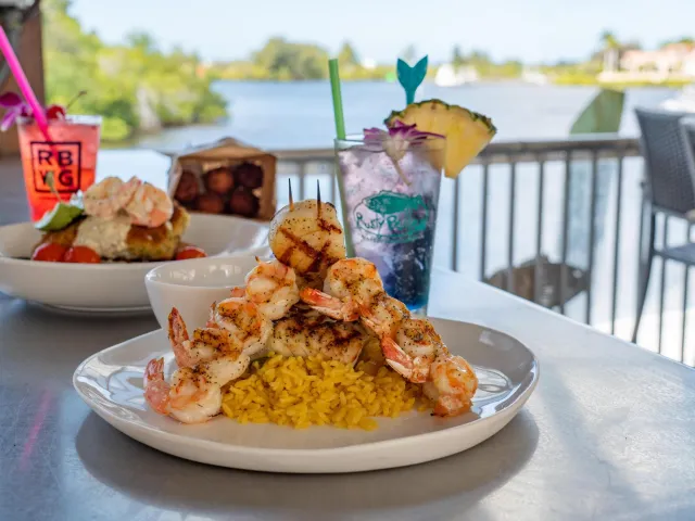 Two seafood dishes and two drinks on a bar overlooking the water at Rusty Bellies.