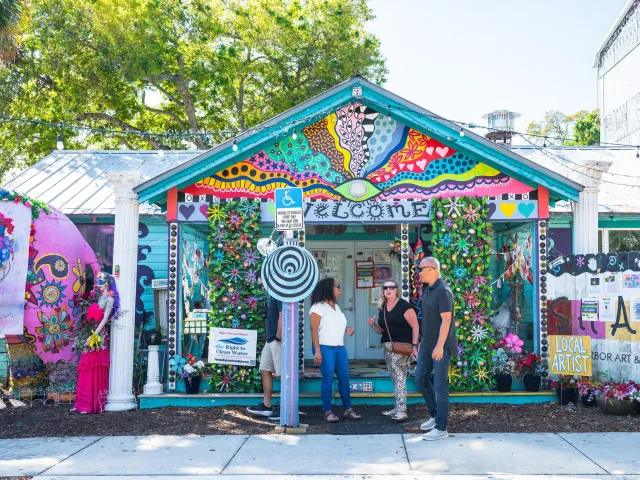 three people stand outside a brilliantly colored and whimsical building