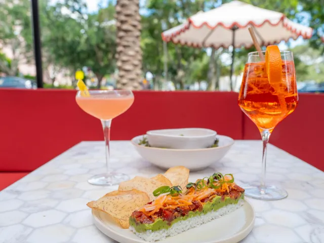 Two cocktails and a plate of food on a table at an outdoor restaurant