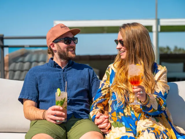 a couple smiles and holds hands and tropical drinks on the rooftop of Hotel Zamora