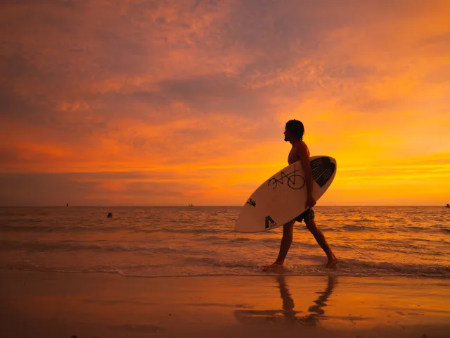 A man walks by the beach at sunset holding a wakeboard in Treasure Island