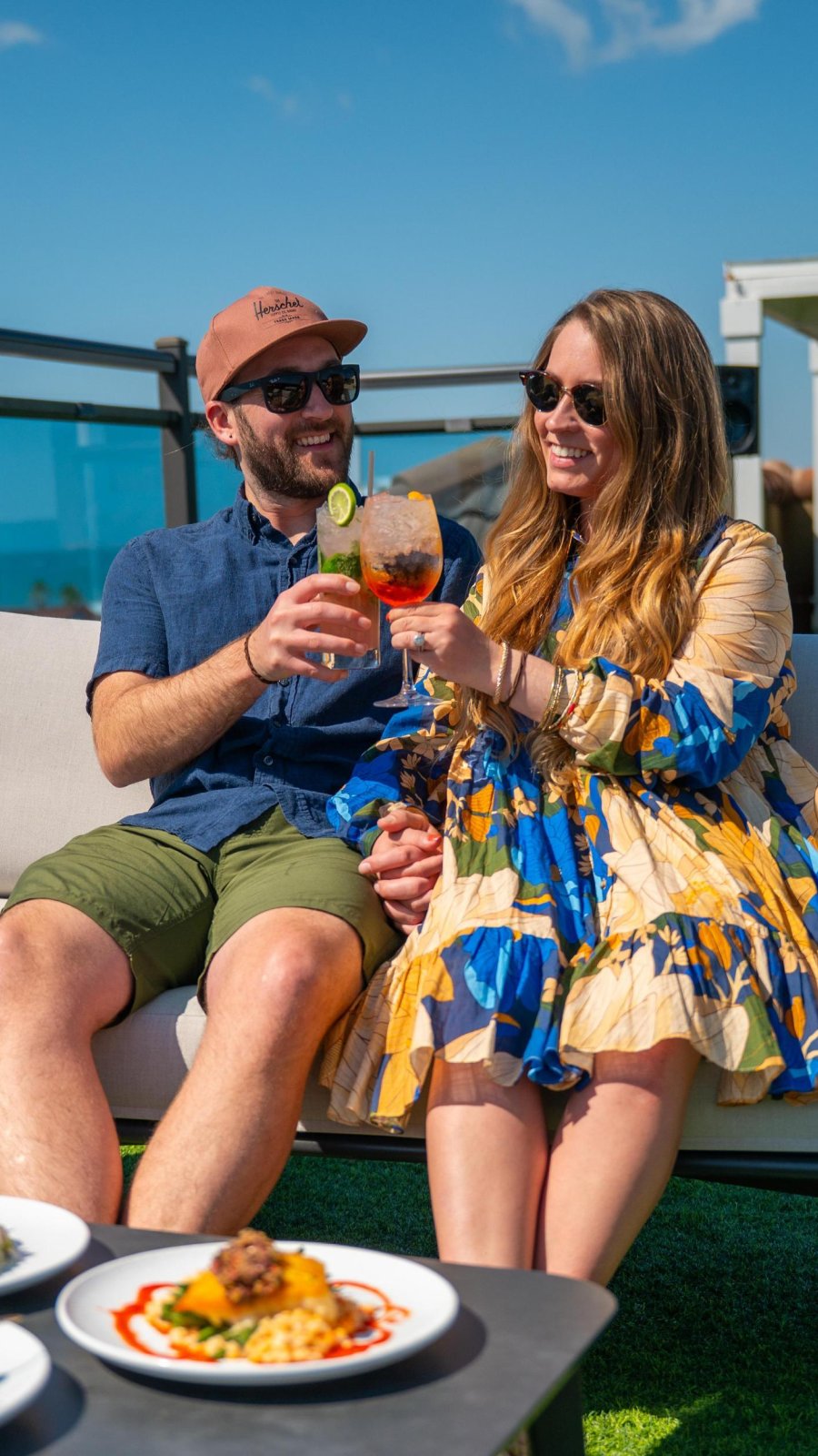 couple sitting next to each other holding cocktails on rooftop deck at The Hotel Zamora