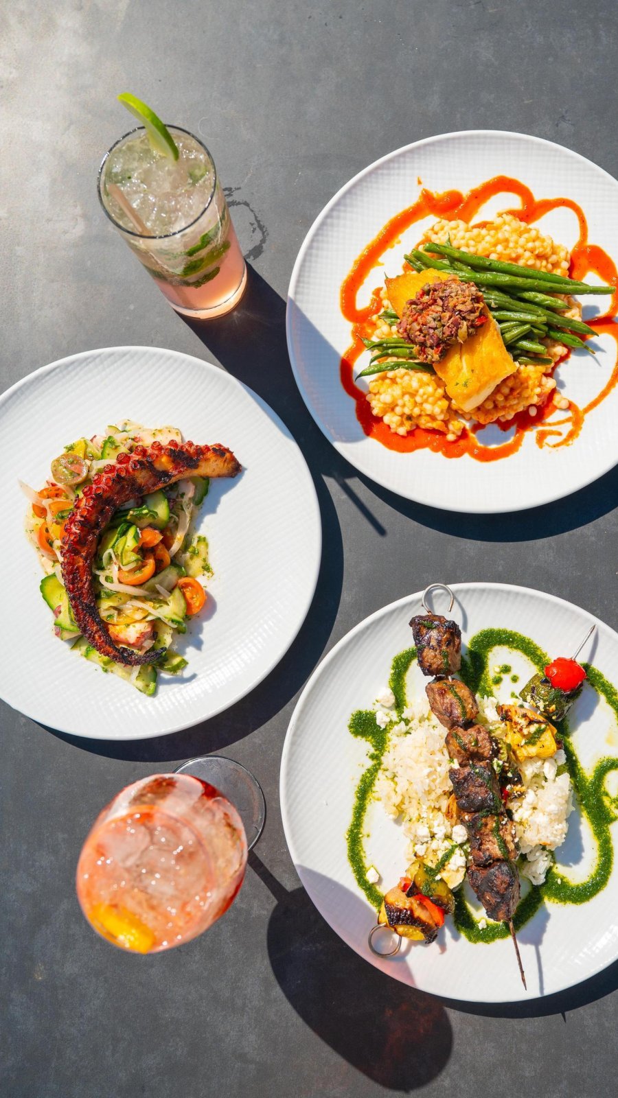 aerial view of three beautifully plated meals and two cocktails on table