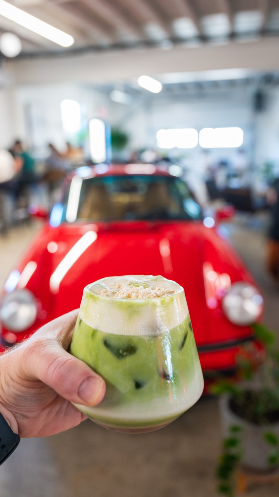 an iced green matcha drink held in someone's hand at Sugar Baby Coffee Concrete in St. Pete; a bright red car is seen on the restaurant's floor