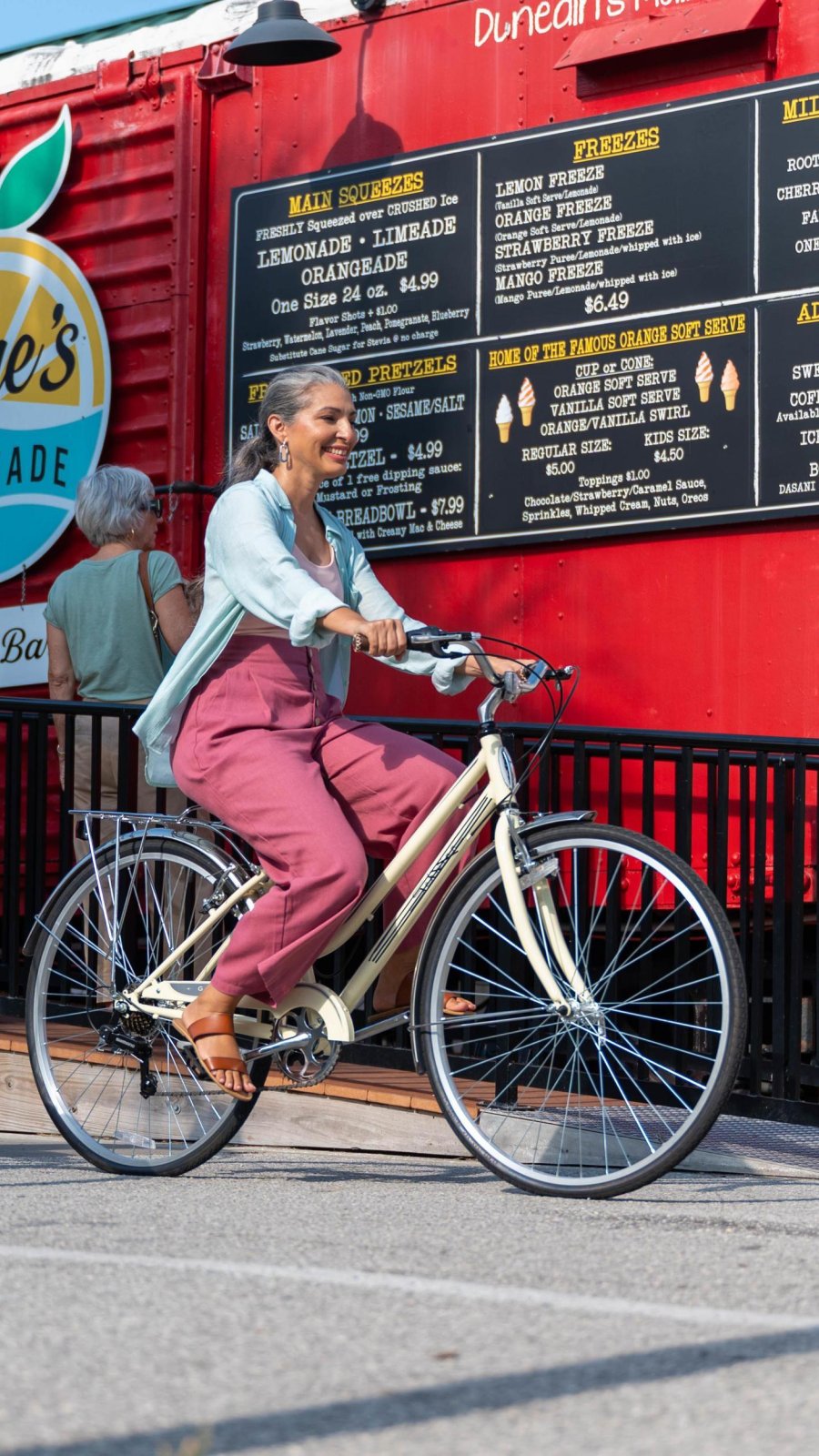 a smiling woman rides a bike past Lane's Lemonade stand in Dunedin FL