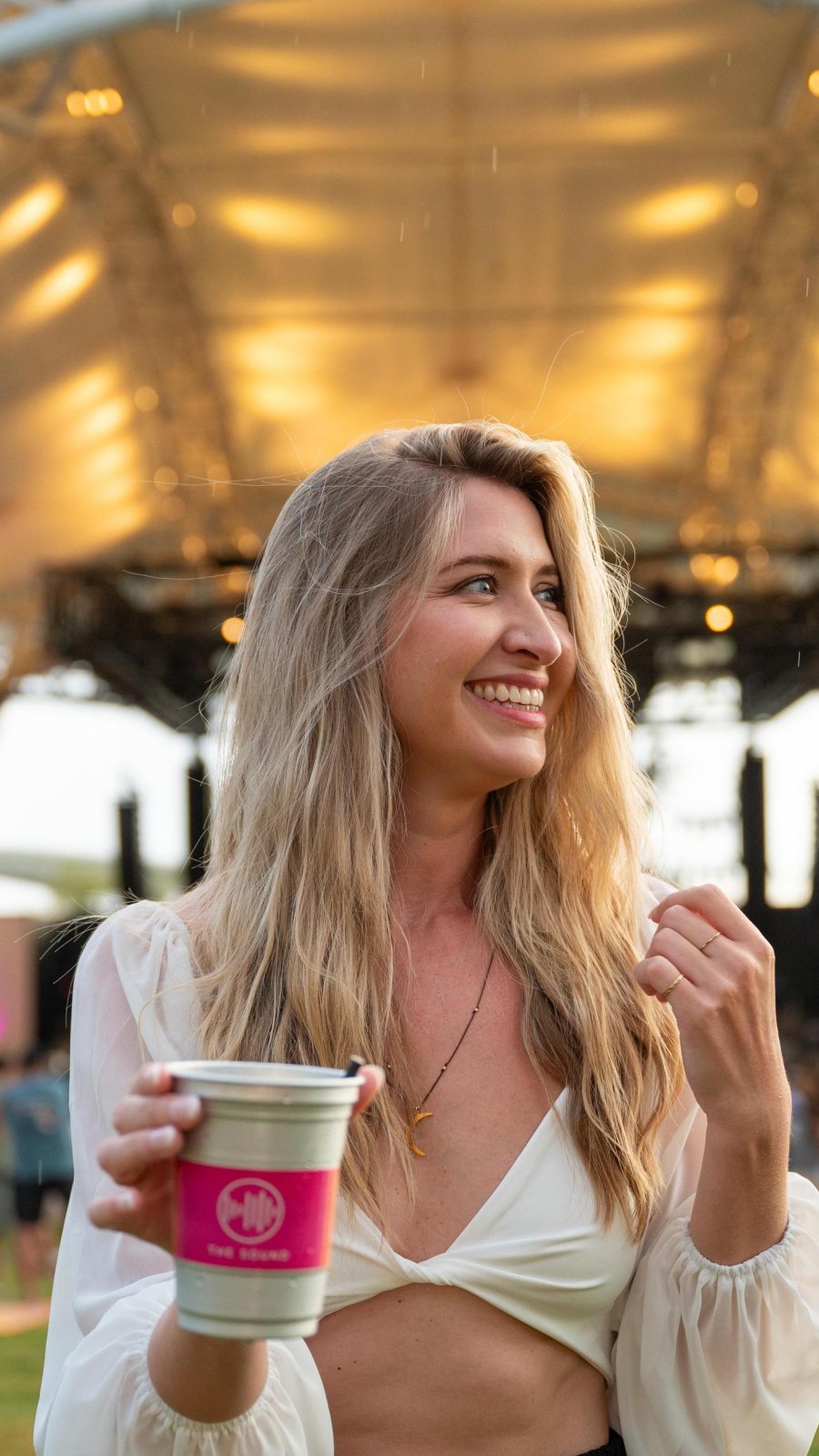 a smiling woman in a white halter top holding a drink at an outdoor concert at the Baycare Sound in Clearwater