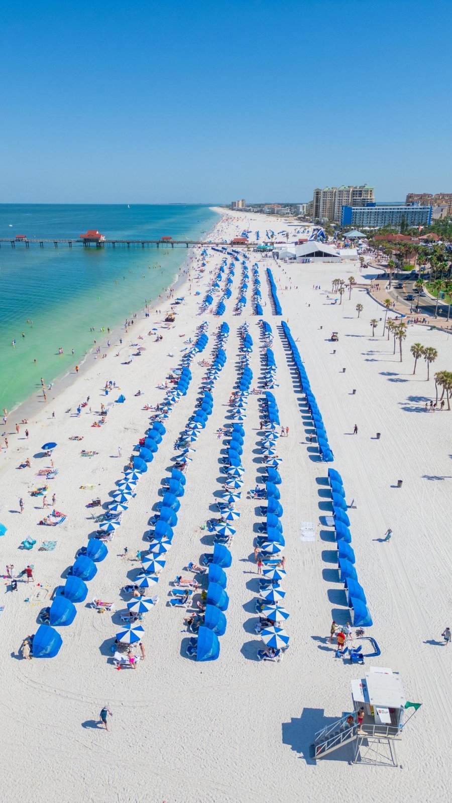 an aerial view of clearwater beach with its white sand, green waters and many blue beach umbrellas
