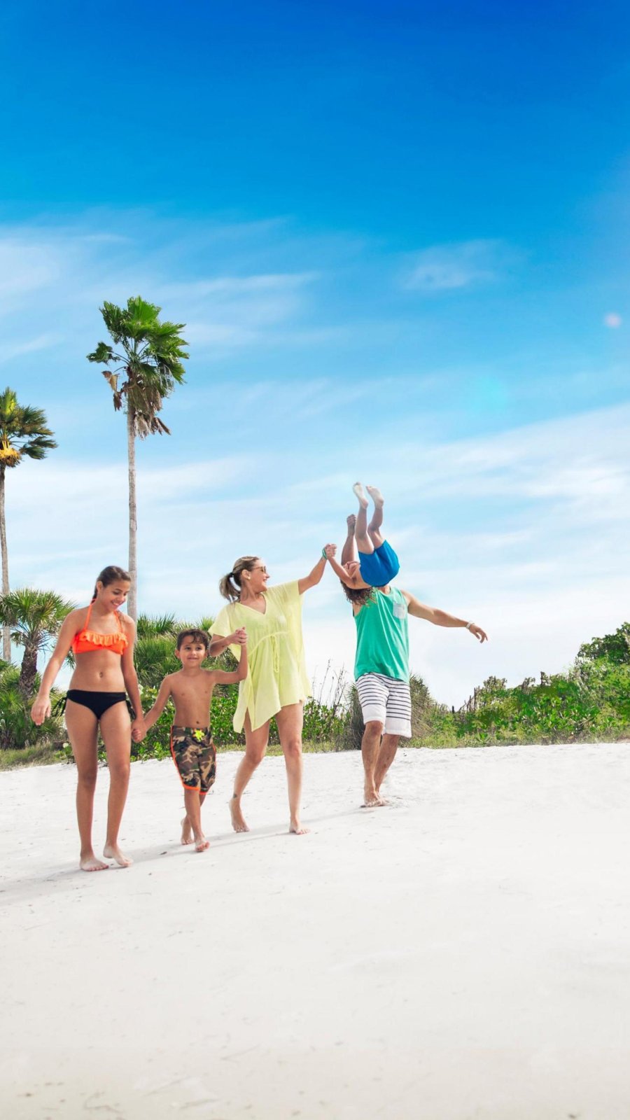 a family goes for a walk on a white-sand beach with palm trees behind them