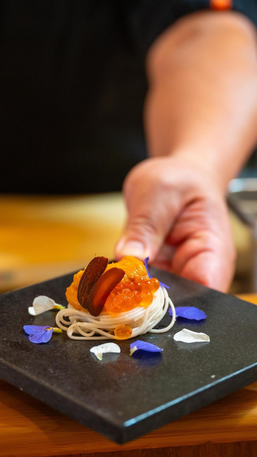 a chef's hand holding out a small plate of artfully presented sushi at Sushi Sho Rexley in St. Pete
