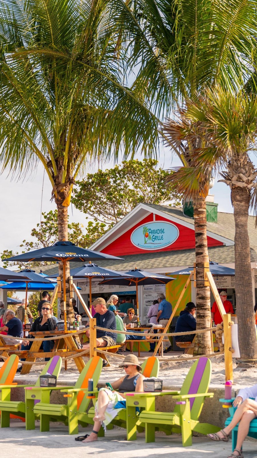 colorful adirondack chairs line the beach with Paradise Grille in the background