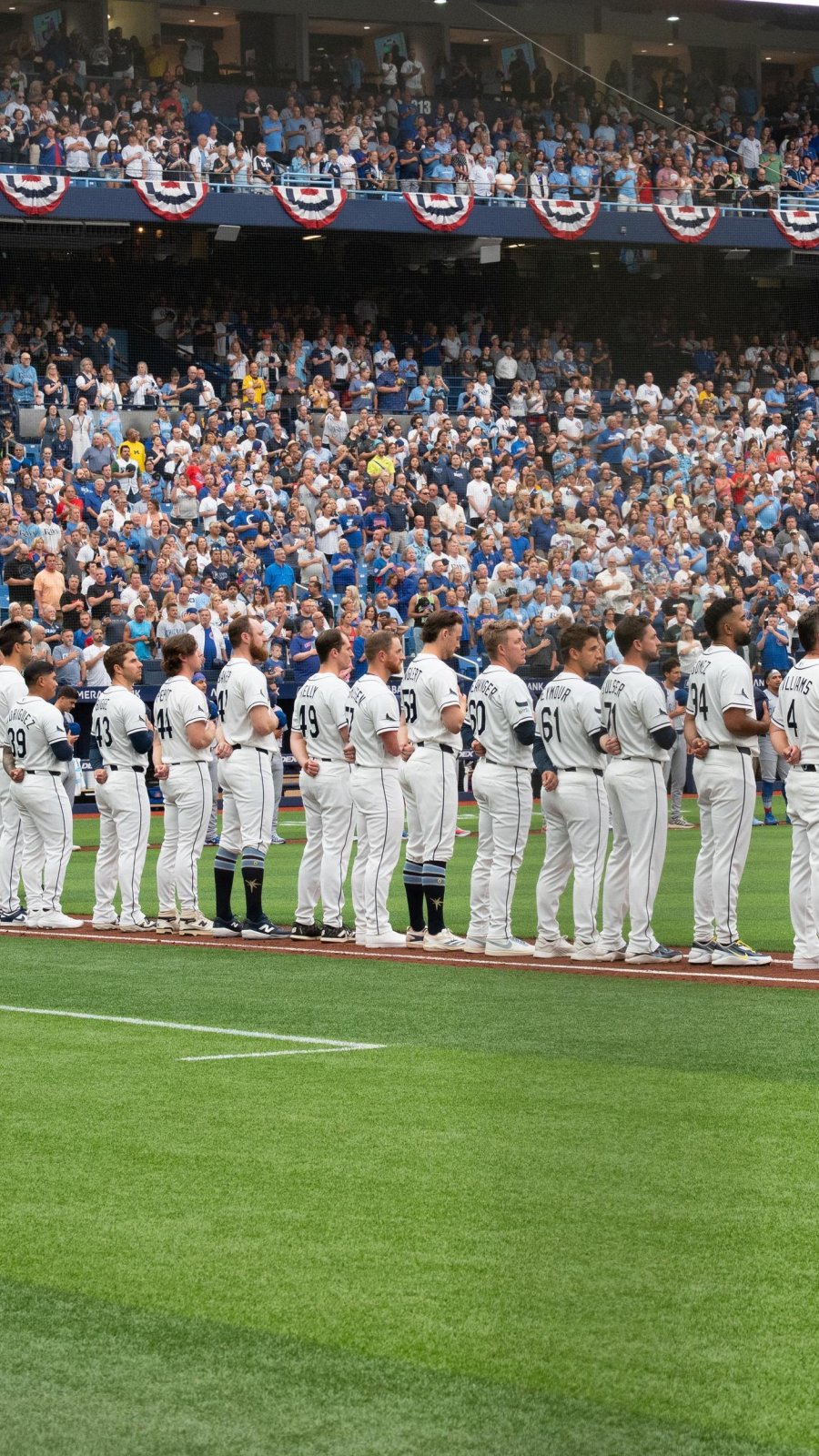 Tampa Bay Rays players line up for the National Anthem, with a crowd in the stands behind them