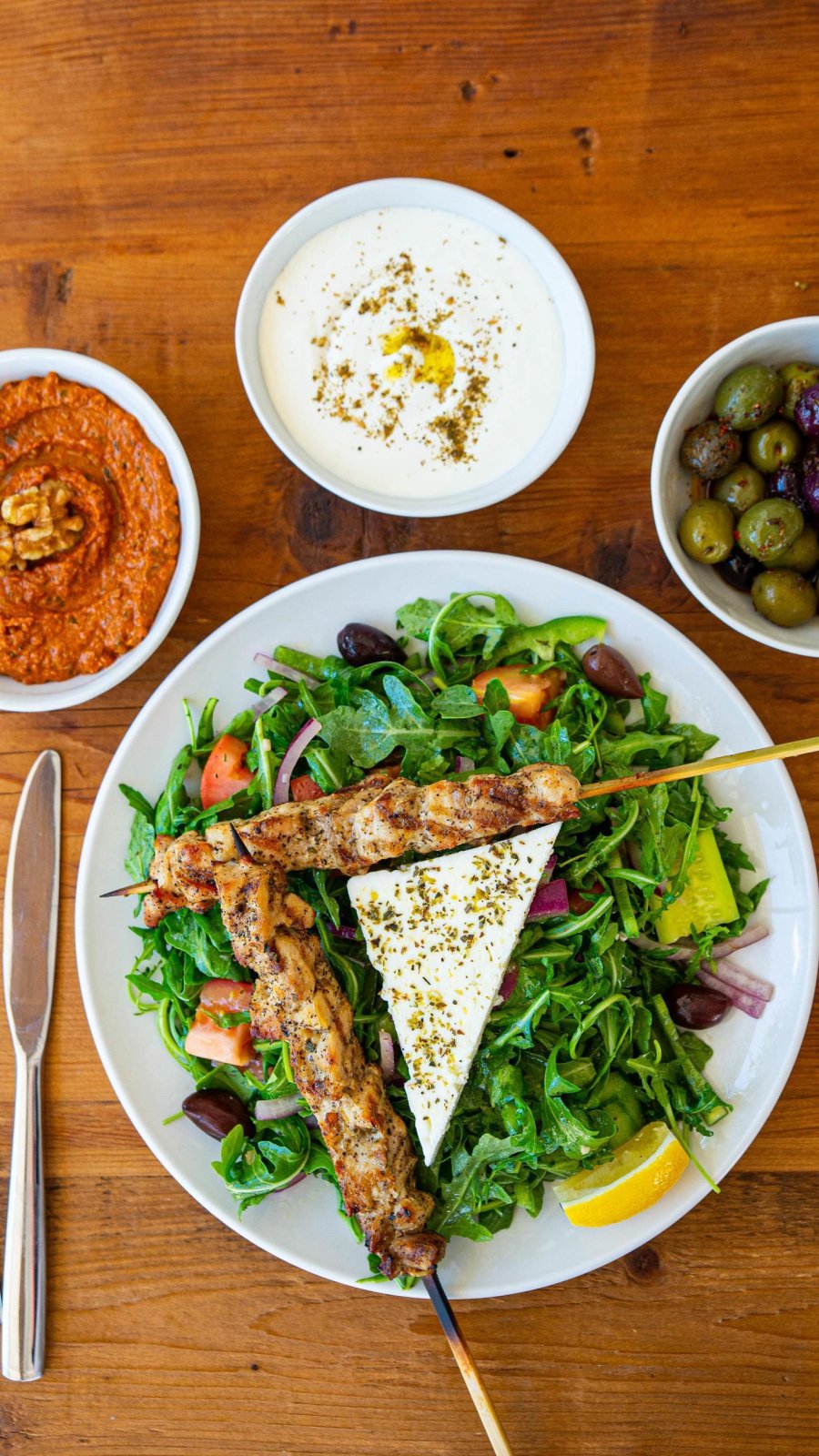 chicken skewers atop a greek salad at Baba on Central in St. Pete FL with olives and dipping sauces on the table