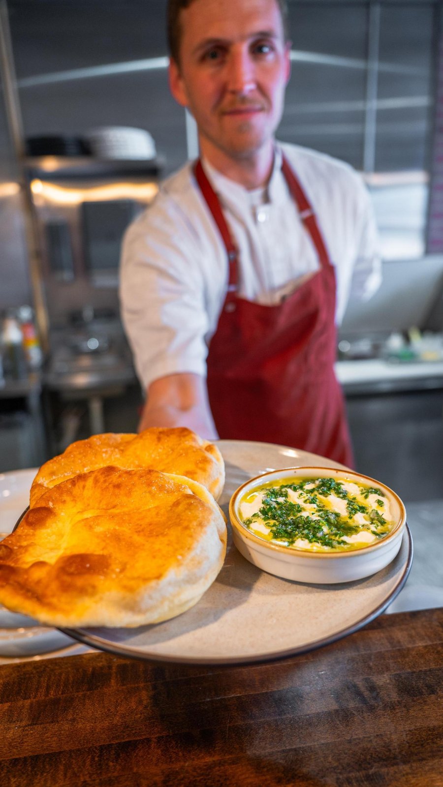 a chef holds out a dish with freshly baked bread and a dipping sauce at The Restorative in Dunedin