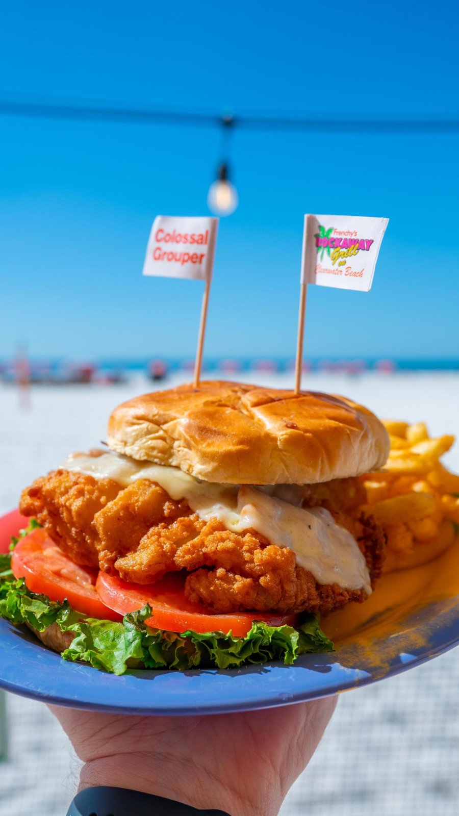 a person holding a plate with a fried grouper sandwich at Frenchy's Rockaway Grill, with a view of Clearwater Beach