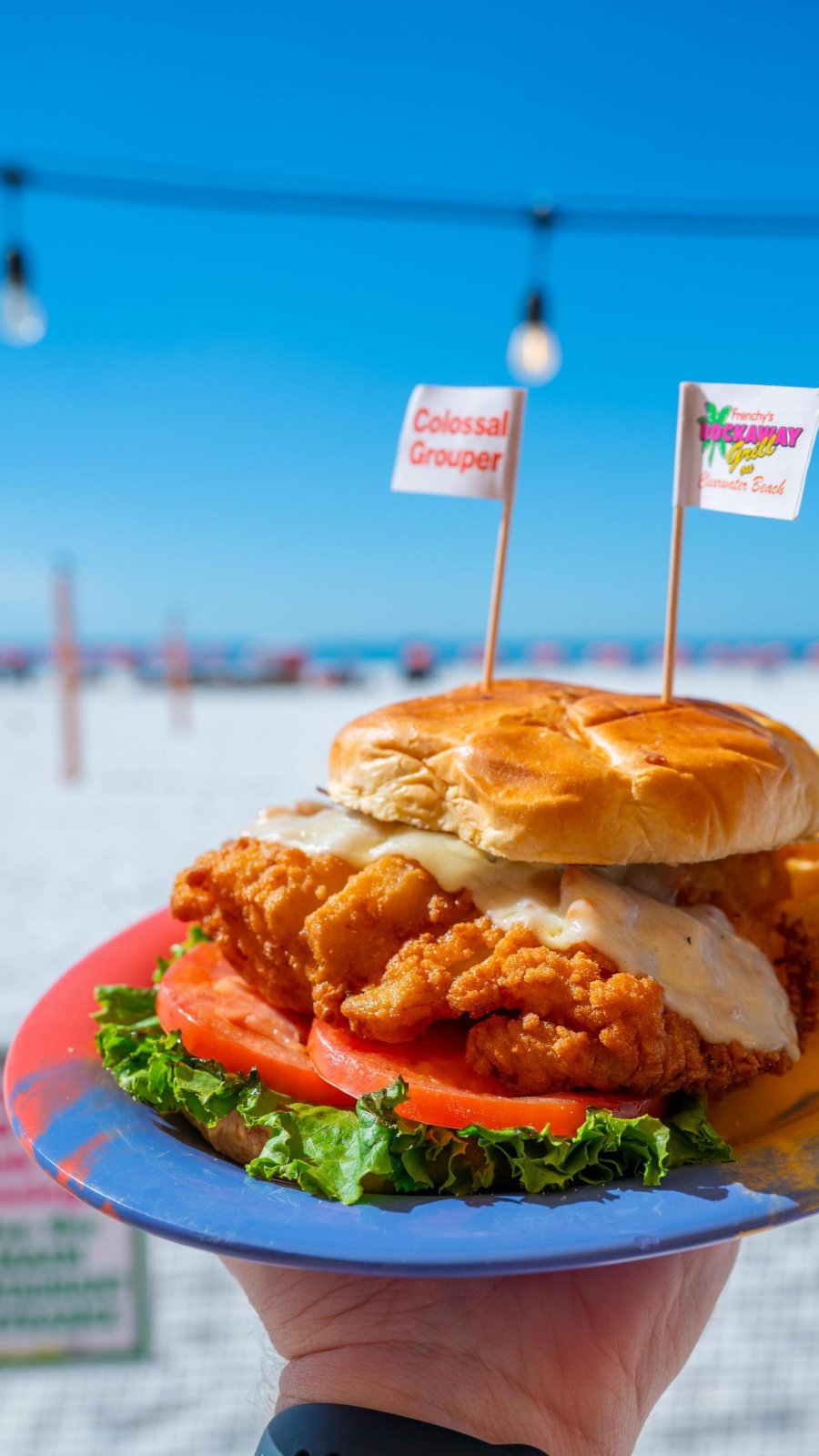a person holding a plate with a fried grouper sandwich at Frenchy's Rockaway Grill, with a view of Clearwater Beach
