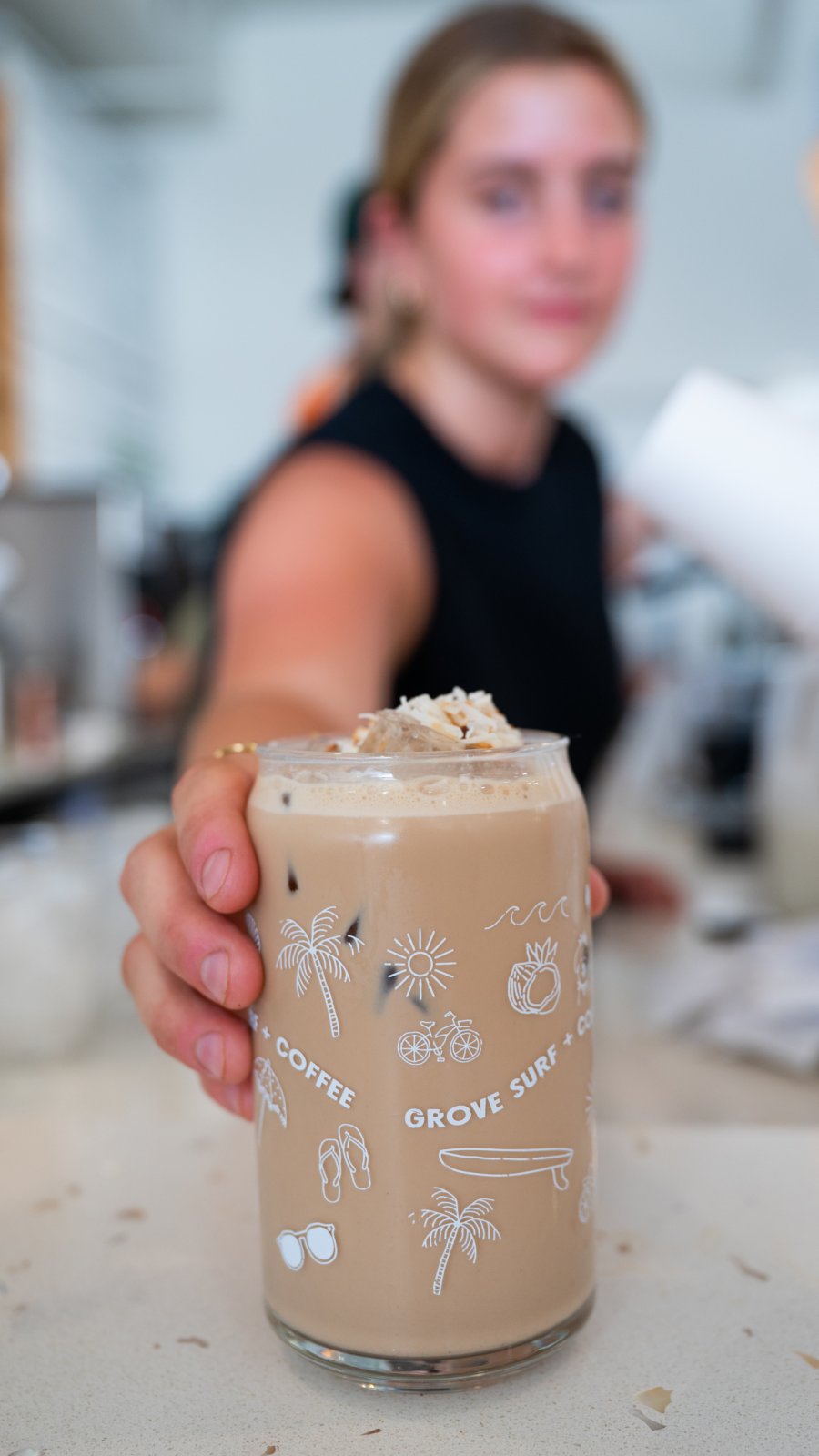 a barista holds out a chilled toasted coconut latte, the signature drink at Grove Surf + Coffee in St. Pete Beach